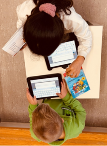 Ein Schüler und eine Schülerin arbeiten in der Grundschule mit einer Lektüre und einem Tablet
